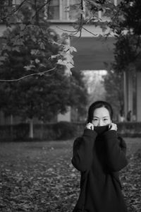 Portrait of woman covering face with turtleneck while standing by tree during winter