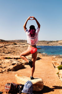 Rear view of young woman posing on rock against clear sky