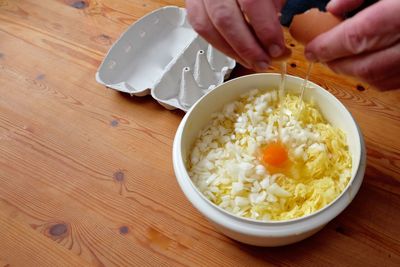 Cropped hands of man breaking egg yolk in bowl on table