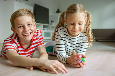 Portrait cheerful siblings playing with dice while lying on carpet at home