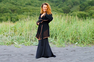 Cheerful mid adult woman wearing black dress at beach