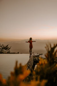 Rear view of woman walking on beach against sky during sunset