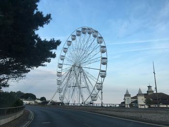 Ferris wheel by road against sky in city