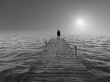 Rear view of man standing on jetty over sea against clear sky