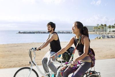 Sporty couple riding bicycles on road by beach