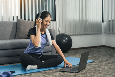 Young woman using phone while sitting on laptop