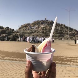 Midsection of person holding ice cream against sky