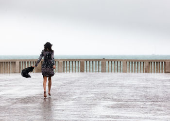 Rear view of woman walking on promenade at beach against clear sky