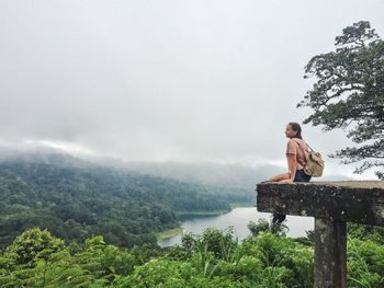 Young woman sitting on observation point in front of river and mountains