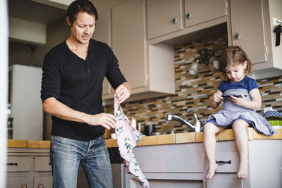 Daughter using phone while father working in kitchen