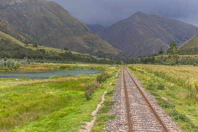 Dirt road amidst field against mountains