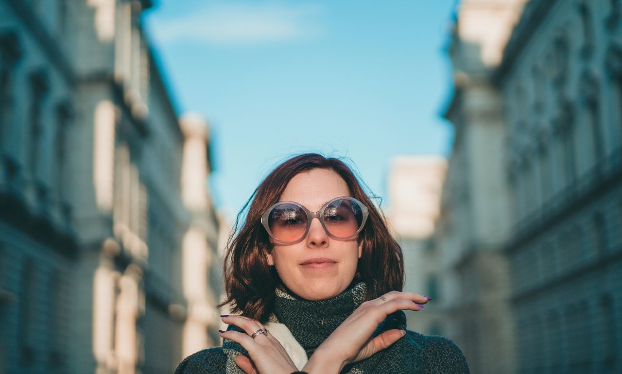 architecture, glasses, one person, city, blue, portrait, adult, women, fashion, young adult, sunglasses, building exterior, city life, built structure, smiling, copy space, headshot, sky, lifestyles, front view, travel destinations, tourism, nature, eyeglasses, hairstyle, happiness, clothing, travel, emotion, focus on foreground, tourist, brown hair, casual clothing, outdoors, looking at camera, leisure activity, day, sunlight, long hair, female, street, person, standing, looking, building, cool attitude, cheerful