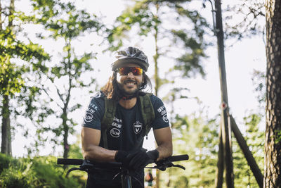 Smiling male cyclist wearing helmet leaning on cycle