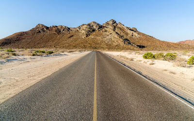 Road leading towards mountains against clear sky