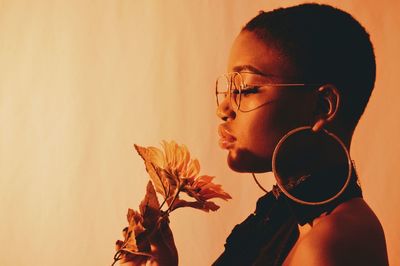 Close-up portrait of young woman with eyeglasses against wall