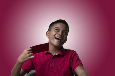 Smiling boy holding card while sitting against pink background