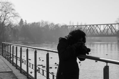 Woman photographing through dslr while standing by lake during winter