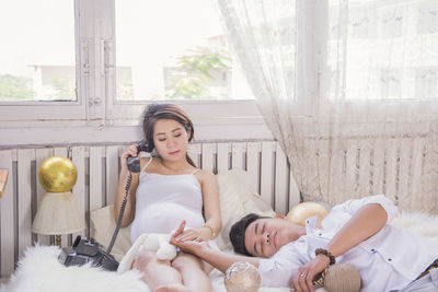 Pregnant woman talking on phone with boyfriend sleeping on bed at home