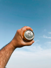 Cropped hand holding navigational compass against blue sky