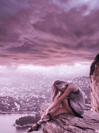 Woman sitting on shore against sky during sunset