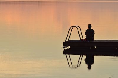 Silhouette man standing on boat in lake against sky during sunset