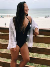 Smiling young woman standing by railing against beach