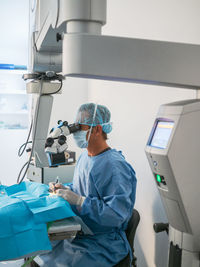 Side view of adult doctor in medical uniform using professional microscope to perform difficult surgery in modern hospital