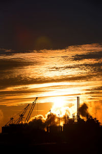 Silhouette of factory against sky during sunset