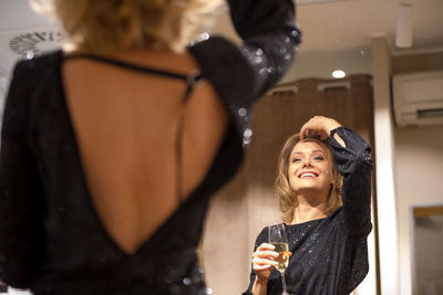 Beautiful and glamorous woman drinking white wine or champagne admiring herself in the mirror