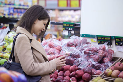 Side view of smiling young woman holding apple in store