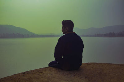 Boy sitting alone near lake.