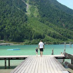 Rear view of man walking with daughter by lake on pier