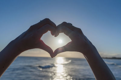 Close-up of hands making heart shape against sea during sunset