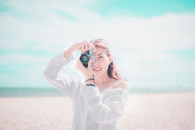 Portrait of woman photographing through camera at beach