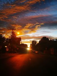 Silhouette city street against sky during sunset