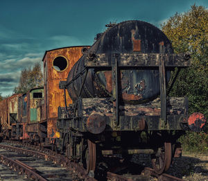 Old abandoned train on railroad tracks against sky