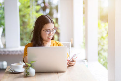 Young woman using phone while sitting on table