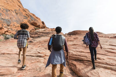 Rear view of friends hiking on rock formations against sky during sunny day