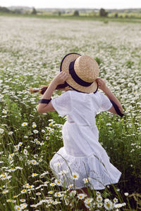 Portrait girl child in a white dress standing on a daisy field in a hat