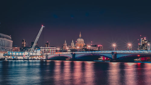 Illuminated bridge over river against sky at night