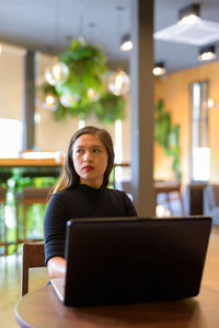 Young woman using phone while sitting on table