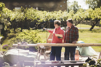 Senior woman showing something to man while holding wooden plank at yard