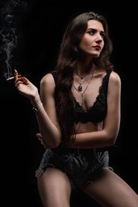 Young woman smoking cigarette against black background