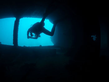 Professional divers swimming near old sunken ship covered with moss on bottom of deep sea with clear water