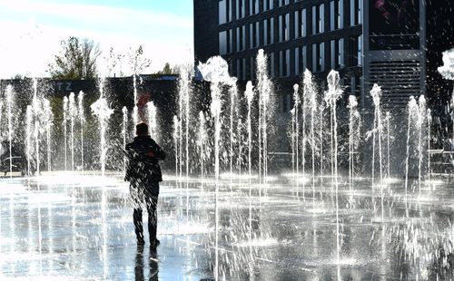 Man standing by fountain against buildings in city