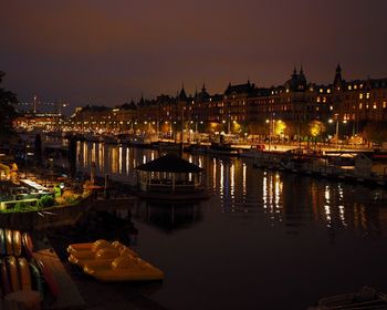 Illuminated buildings in front of river against sky at night