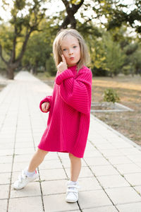 Cute funny child girl 4-5 year old wear bright pink sweater having fun playing in park outdoor. 
