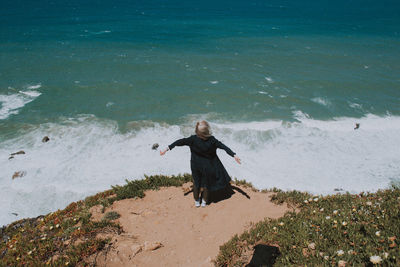 Rear view of woman standing on cliff by sea