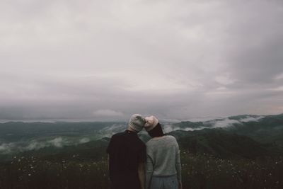 Rear view of couple standing on mountain against sky during winter