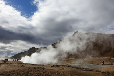 Tourists on landscape against cloudy sky